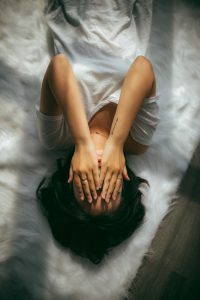 girl lying on the bed with hands covering her face 