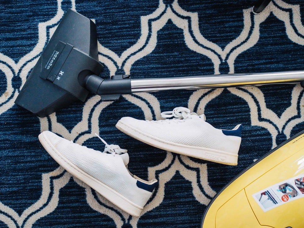 Blue Carpets with white design, Vaccum Cleaner head and Two white shoes placed sideways on the carpet 